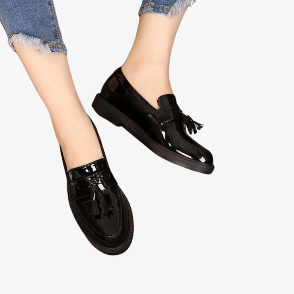 Women's black patent loafers, elegant and glossy. These shoes are adorned with decorative tassels on top, adding a classic, sophisticated touch. Their timeless design is perfect for a chic, relaxed look.