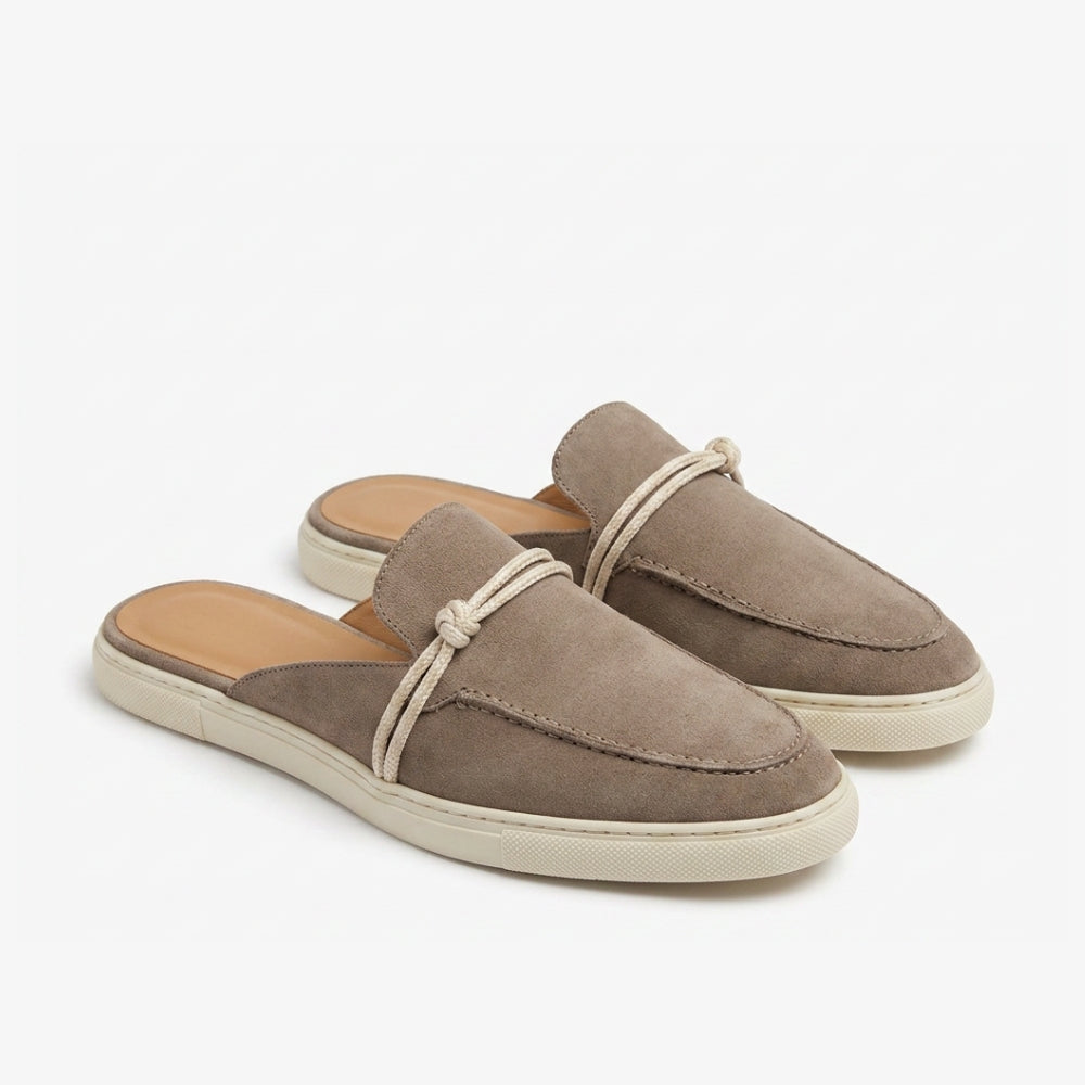 Genuine suede leather mule loafer in taupe brown with a beige sole and strap, on a gray background