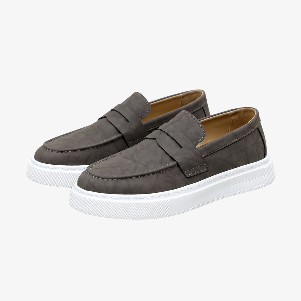 Men's brown leather loafer with a white sole, on a gray background Image