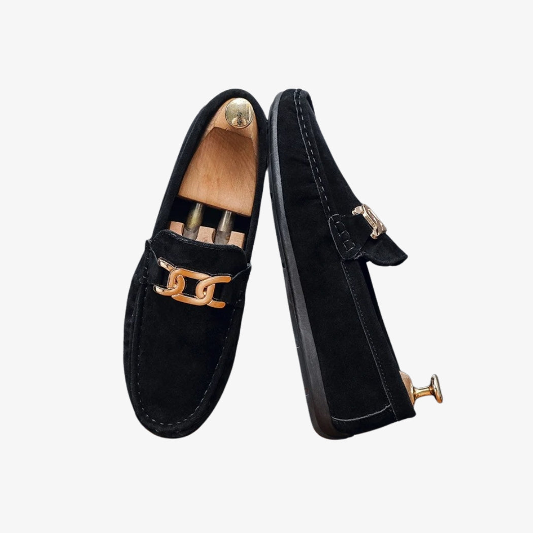 Men's black faux suede loafers, elegant and modern, with a gold metal buckle on top. Their refined design shows visible stitching that adds a touch of character. The black sole completes their sober, chic look.