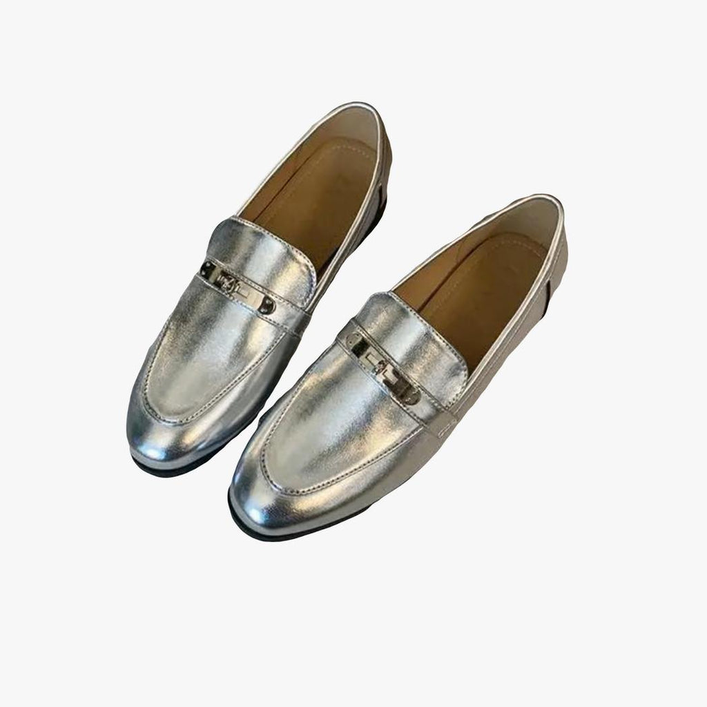 on a light background, a pair of silver block heel loafers for women