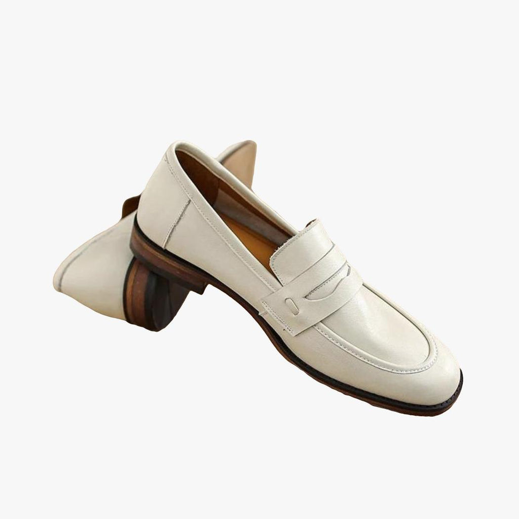 A pair of beige genuine leather loafers with brown soles resting on a wooden log