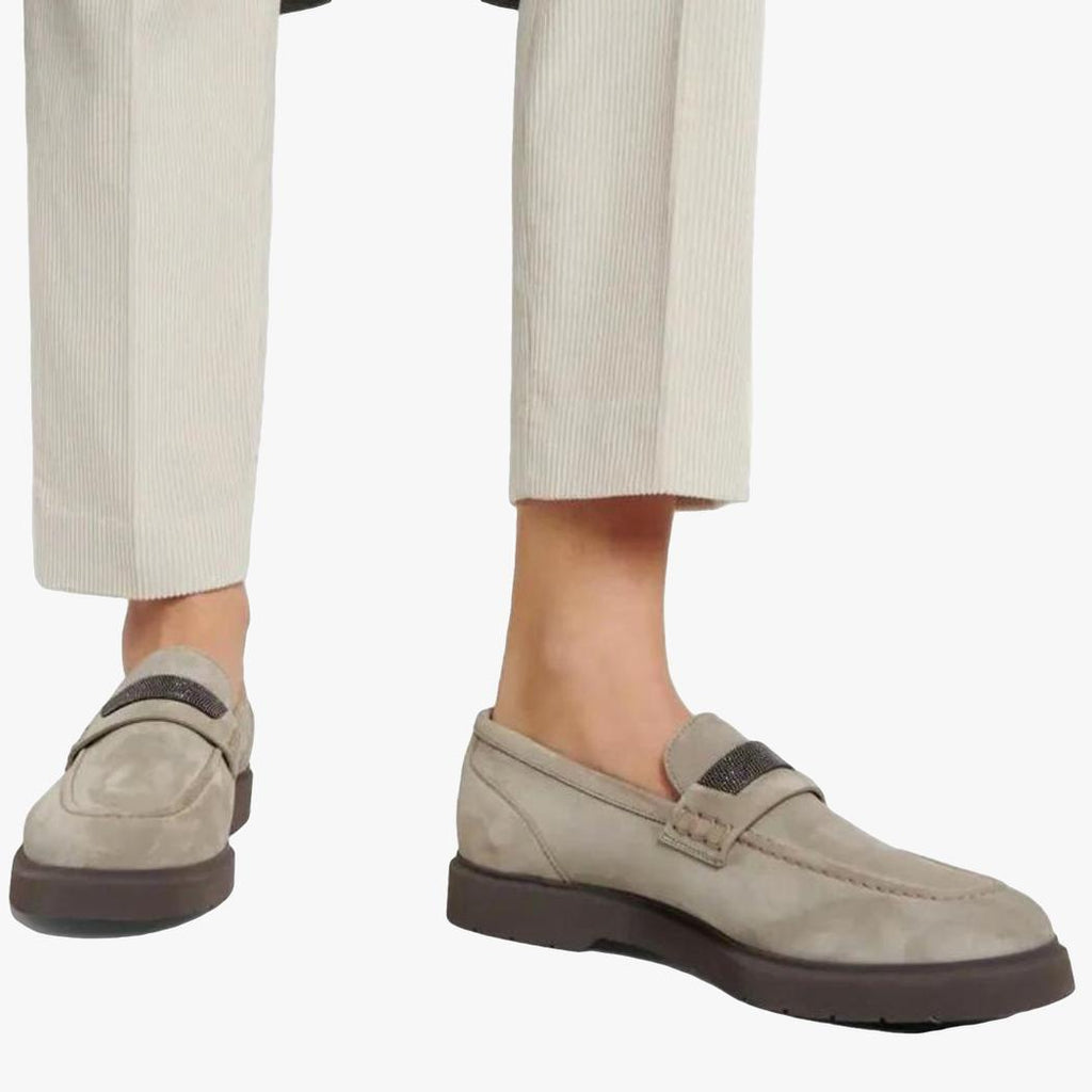 A woman's feet in beige tailored pants and gray genuine suede loafers