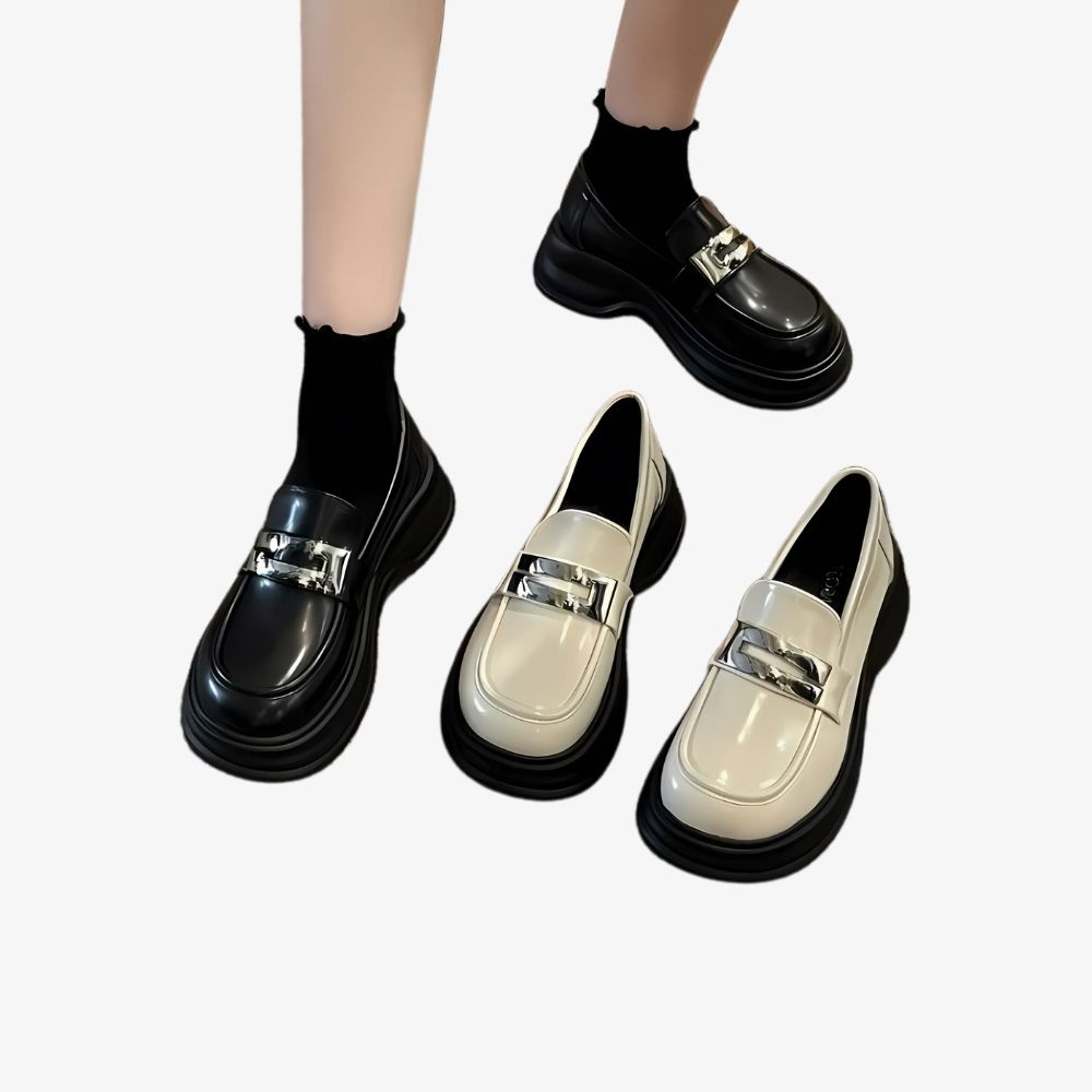 A woman's legs in black platform loafers, with a pair of the same shoes in beige beside them