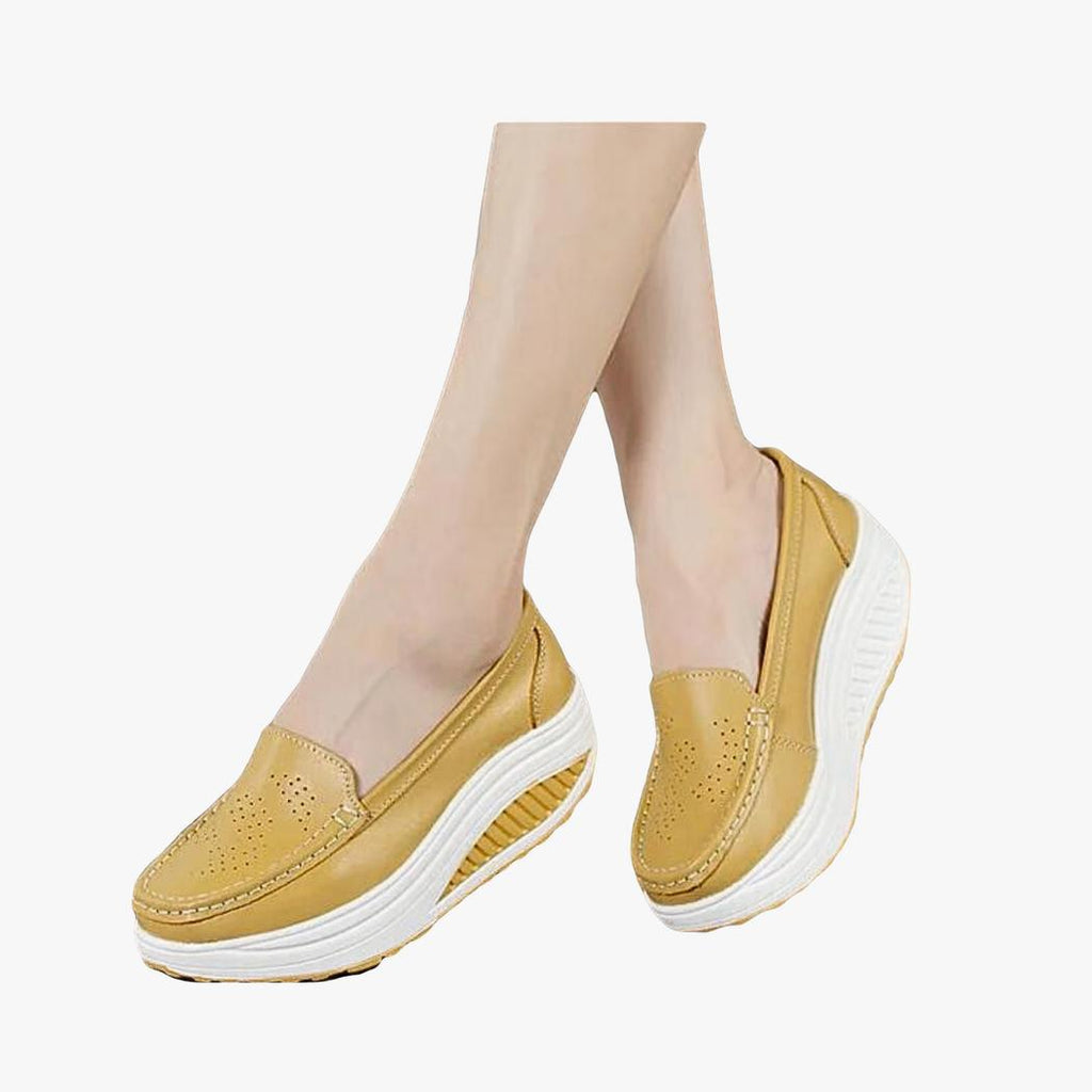 A woman seen only from the feet down, wearing breathable colorful platform loafers in camel