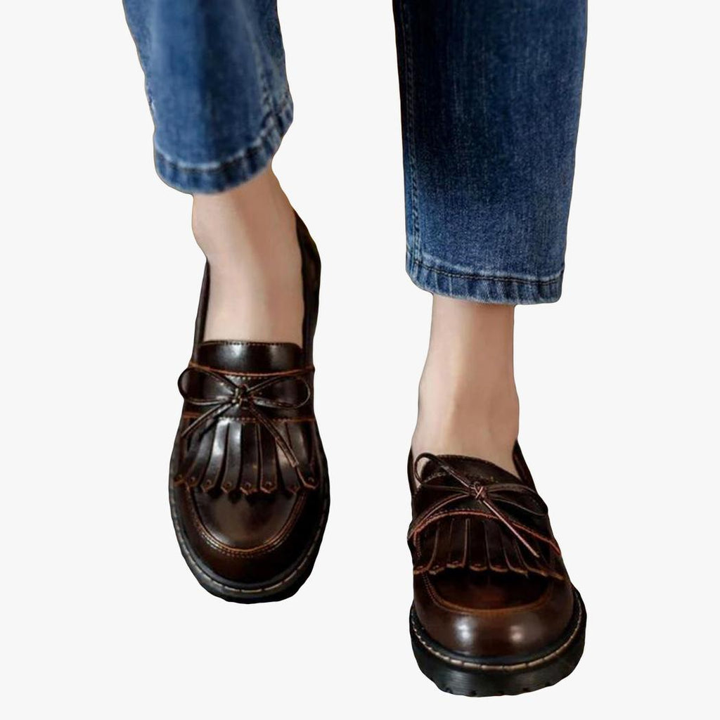A woman's feet in jeans, wearing brown vintage-style square heel loafers with fringe
