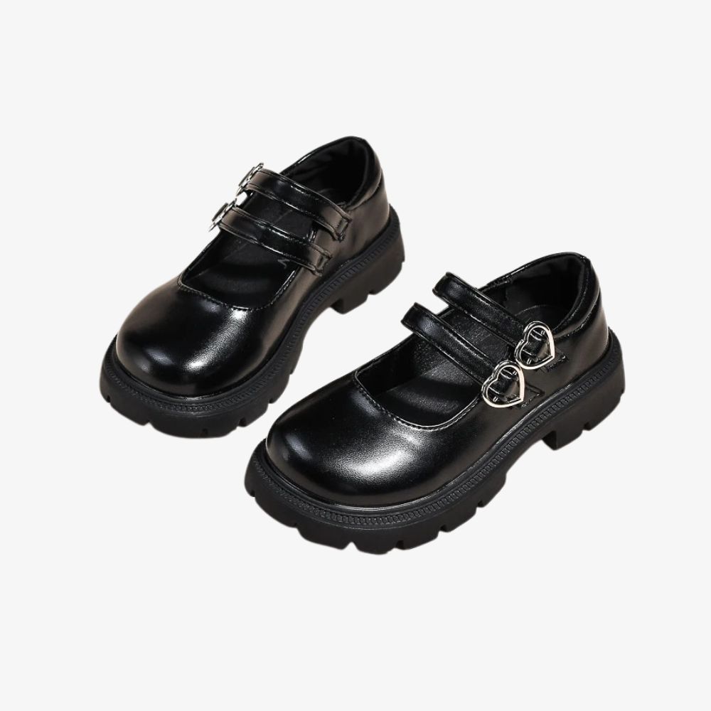 Pair of black loafers with a double strap and a heart detail on top, on a gray background.