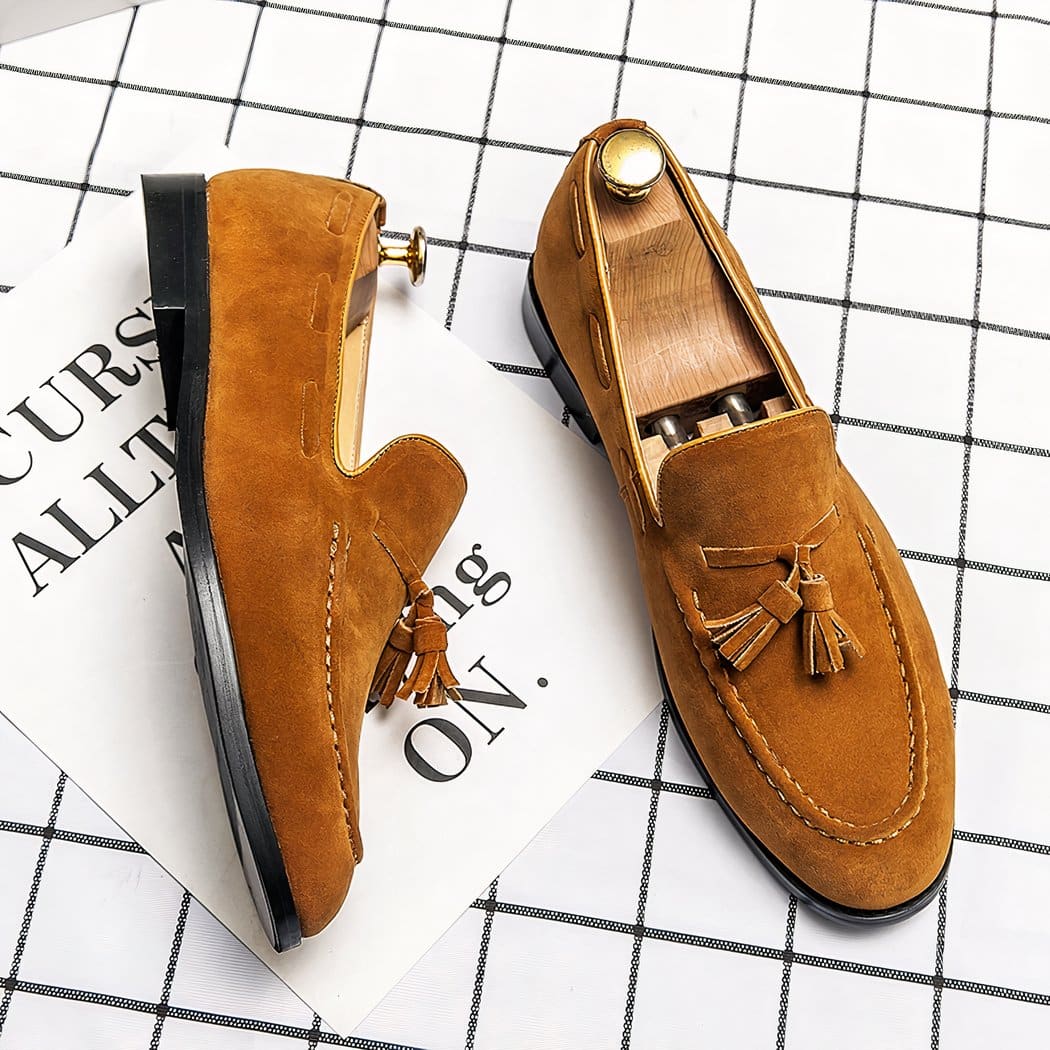 Pair of yellow loafers with tassels on a white checkered surface.
