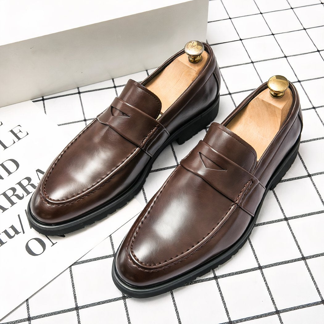 Brown leather loafer on a checkered floor with a leaf and writing next to it