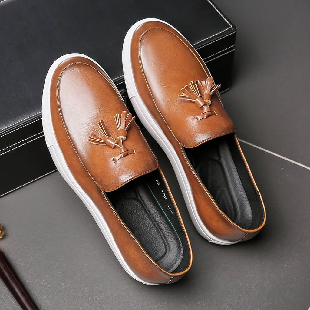 Pair of brown loafers with tassel and thick white soles on grey ground
