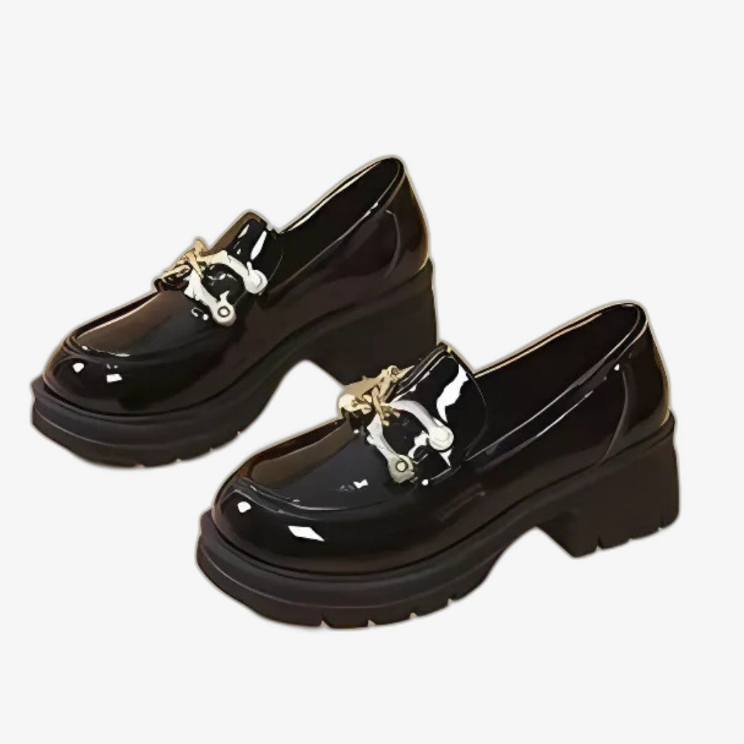 Women's black patent loafers with a chic, modern style. With thick heels for a confident look and good stability, they are adorned with an elegant silver metal buckle on top, adding a refined touch to their glossy design.