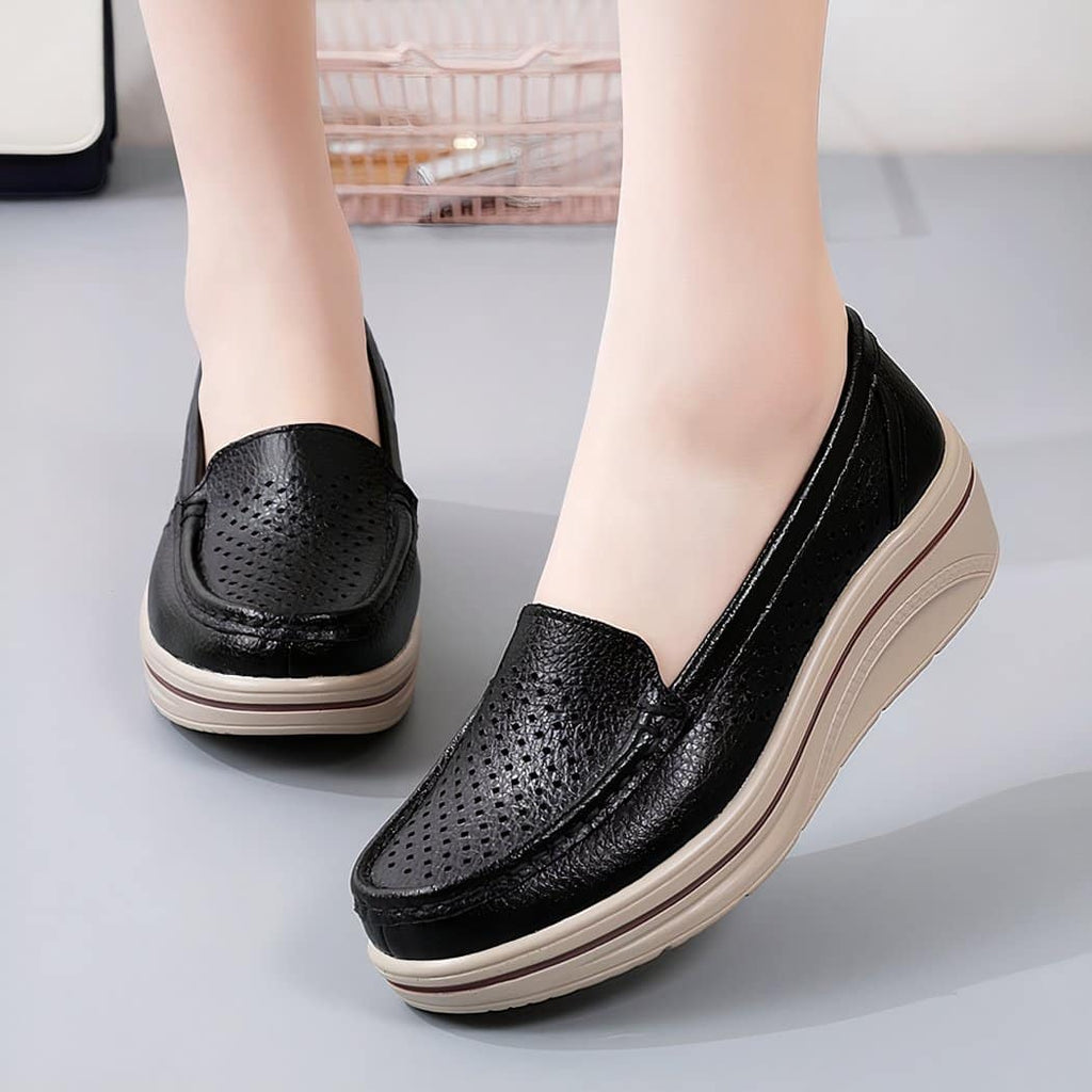 Photo of a pair of black leather loafers worn by a woman on a gray floor