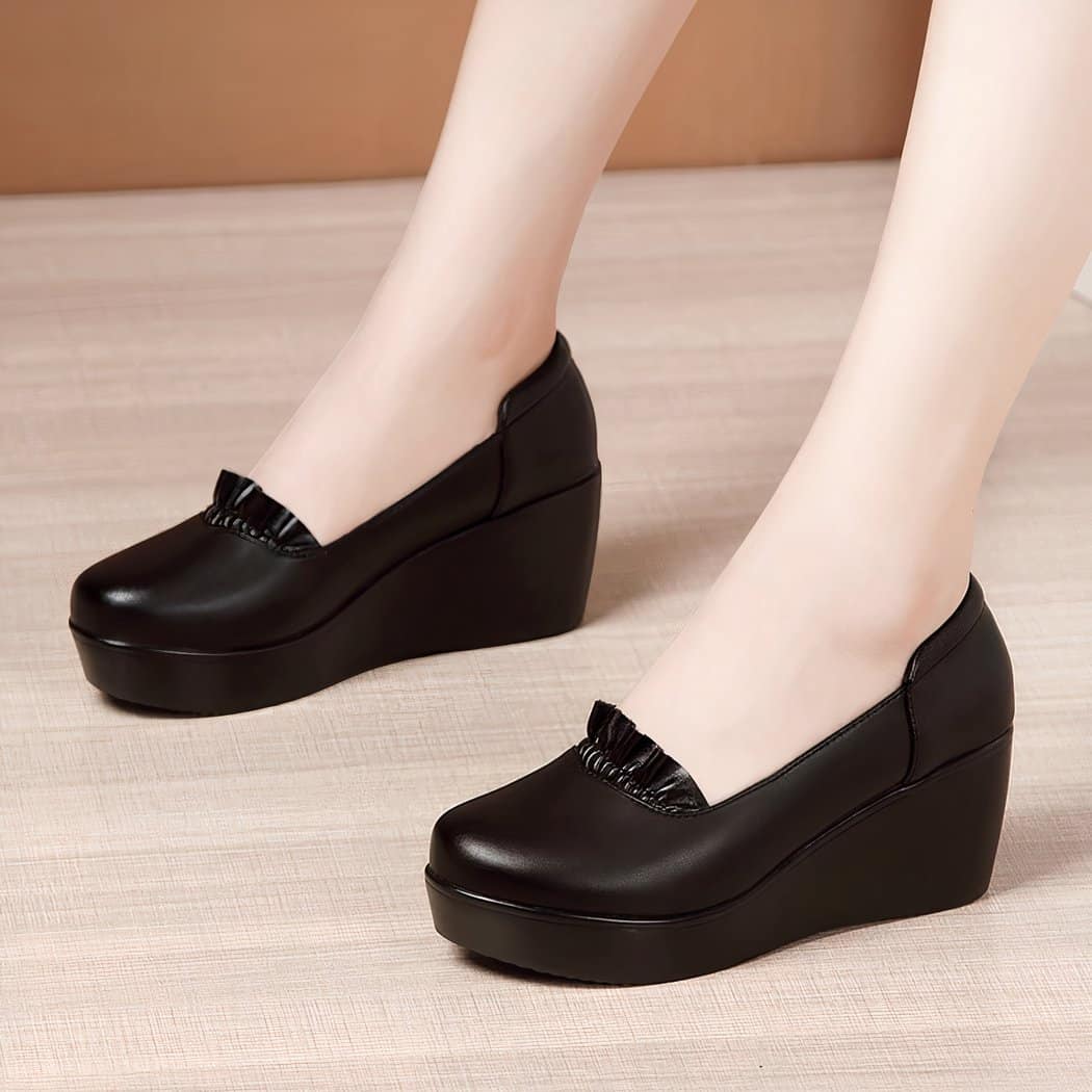 Photo of a pair of black wedge loafers worn by a woman on a parquet floor with a brown wall in the background