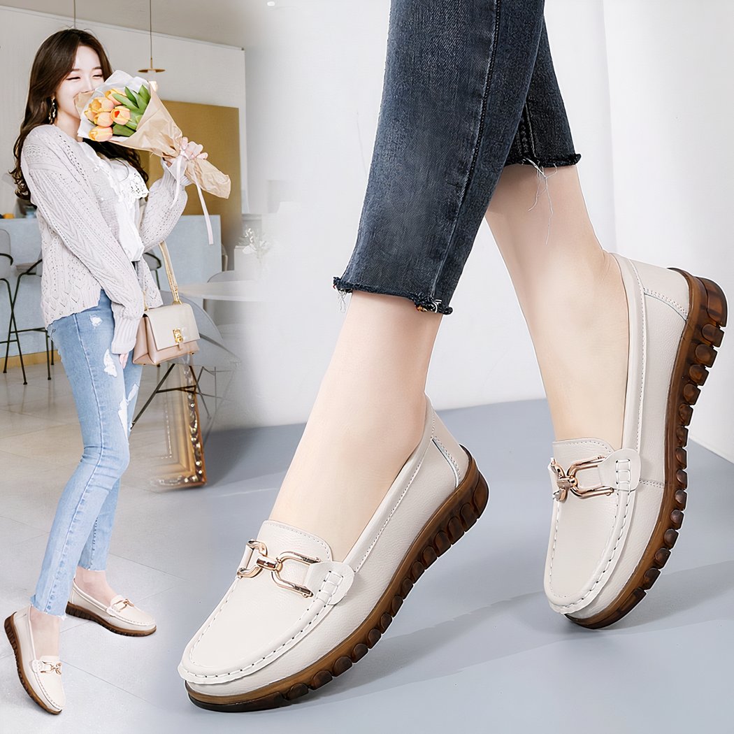 Photo of a pair of white loafers worn by a woman with black jeans, on a gray floor with a woman in the background