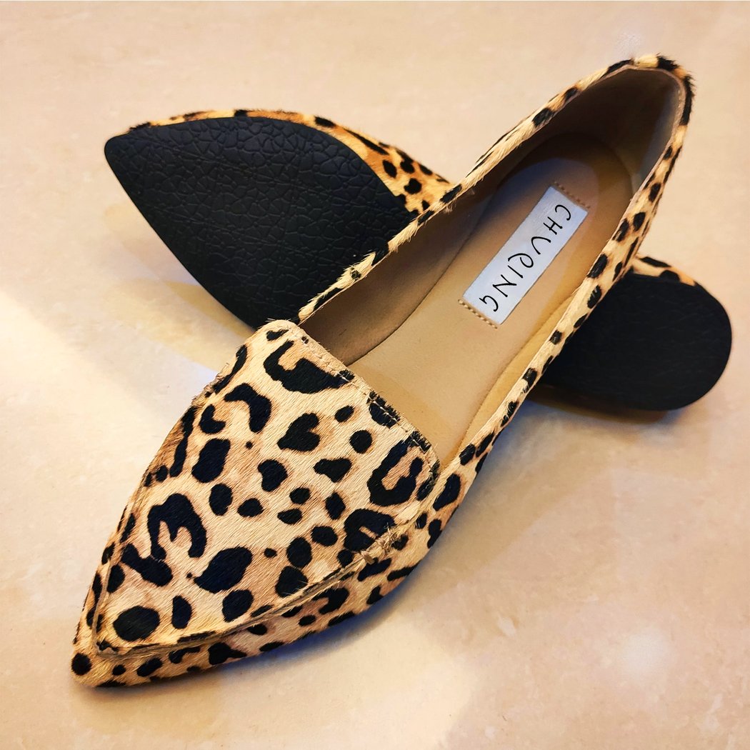 On a marbled pink background, a pair of pointed loafers in suede and brown leopard print.