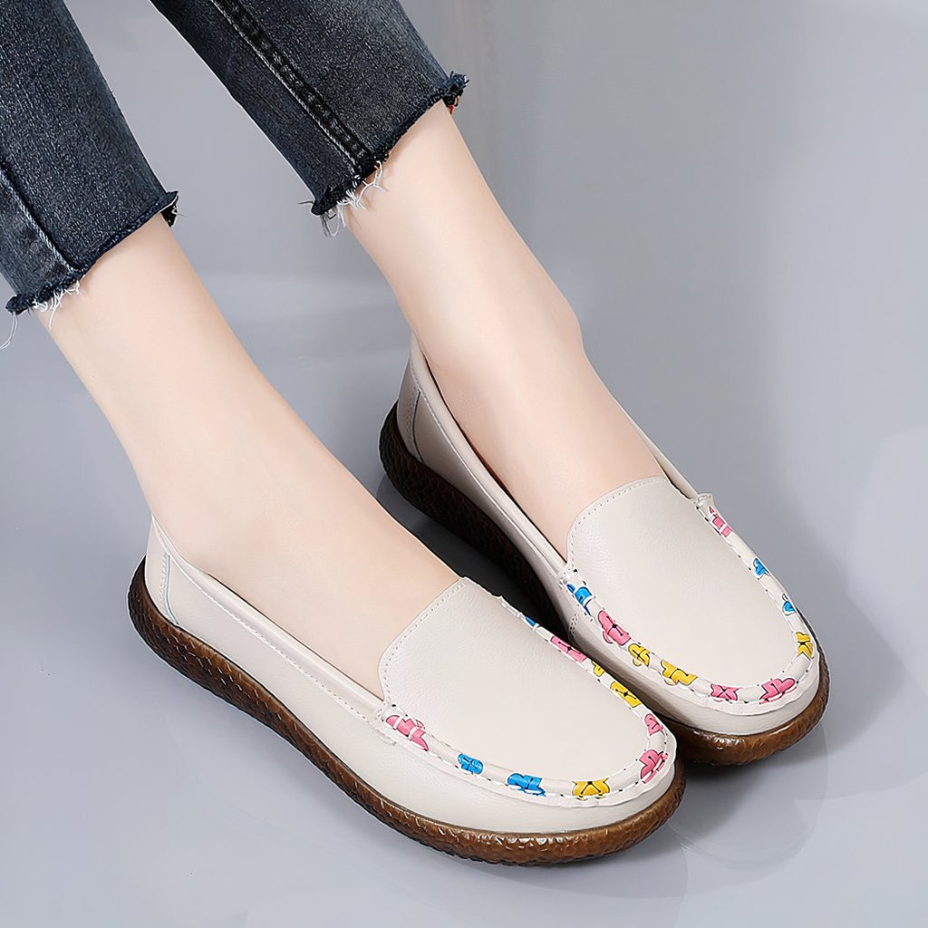 Photo of a pair of beige loafers worn by a woman in black pants, against a gray background