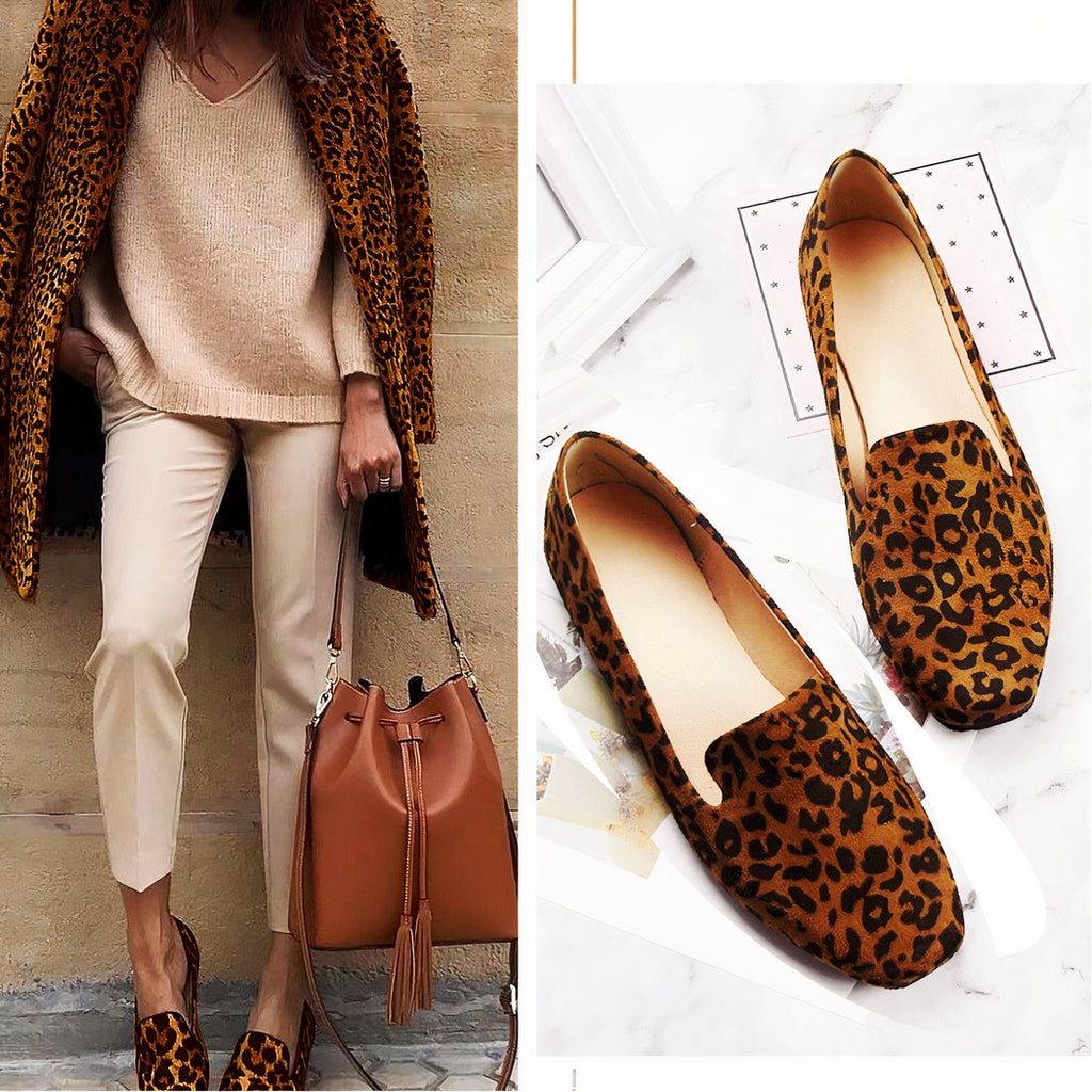 standing woman dressed in beige with bag in hand and wearing leopard loafers