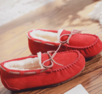 Photo of a pair of red lined suede moccasins on a wooden cabinet.