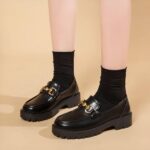 Photo of a pair of black platform loafers worn by a woman on a beige background