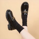 Photo of a pair of black platform loafers worn by a woman on a beige background