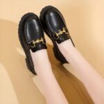 Photo of a pair of black platform loafers worn by a woman on a beige background