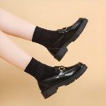 Photo of a pair of black platform loafers worn by a woman on a beige background