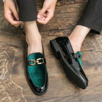 Pair of men's moccasins in black patent on the turn and shiny green velvet with gold bit on the top. They are worn with black pants on a brown parquet floor