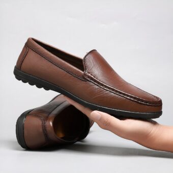 brown leather moccasin held in a man's hand with the other pair of shoes behind it