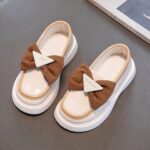 moccasin in white faux leather with a brown bow on a grey background