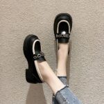 Photo of a pair of black platform loafers worn by a woman in jeans on a beige floor