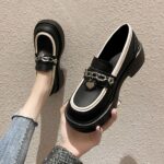 Photo of a pair of black platform loafers worn by a woman in jeans on a beige floor