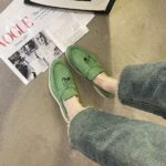 green suede moccasin worn by a woman with a book in front of her feet