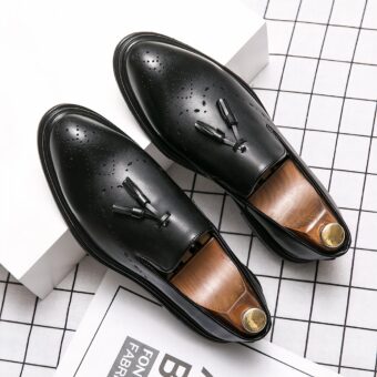 Pair of black leather tassel loafers on a white shoe box