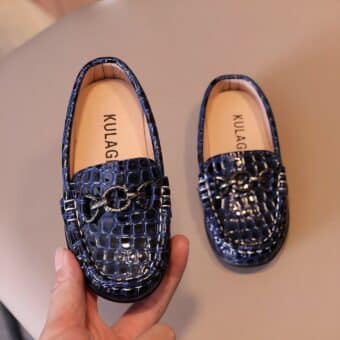 crocodile pattern faux leather baby moccasin with ring on top, these shoes are presented in a woman's hand