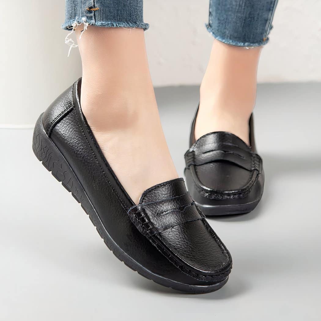 Photo of a pair of black leather moccasins worn by a woman on a gray floor