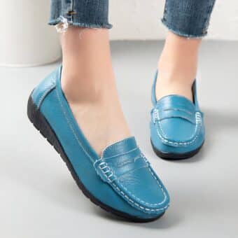 Photo of a pair of blue leather moccasins worn by a woman on a gray floor