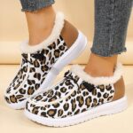 Worn with blue jeans, a pair of white winter moccasins with leopard print and exposed beige fur trim. The sole is thick white and there are decorative black laces on the top of the shoe