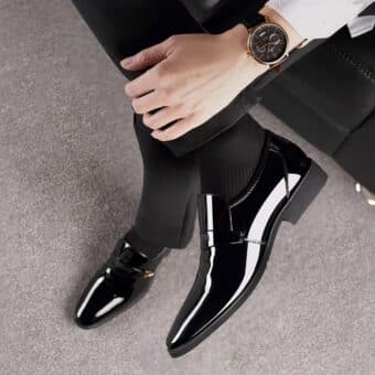 Feet in black patent leather moccasins. Leg crossed with a watch on the wrist.
