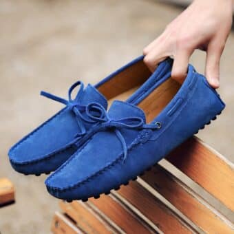 Pair of blue moccasins held in one hand on a wooden bench