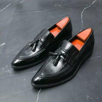 Black loafers with crocodile-skin-look tassel on black floor