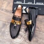 Black loafers with a gold band on the top and a hanging tassel