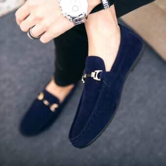 Feet of a person wearing blue moccasins with a gold buckle on the front and wearing a watch on the wrist
