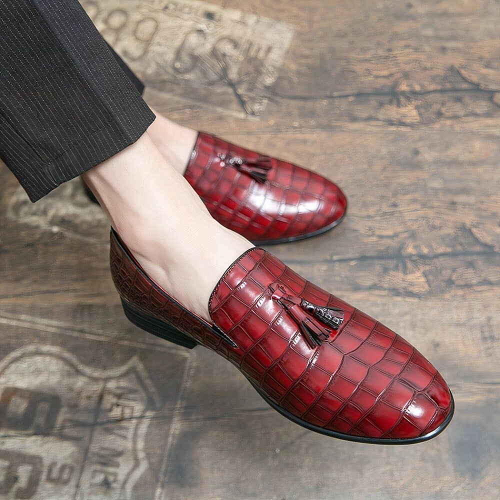 Feet wearing red crocodile-effect moccasins with a tassel on top of the shoe