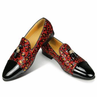 On a white background, a pair of moccasins with the front in black patent, the rest of the shoe in leopard pattern sequin in red with tassels on top. The interior is beige