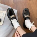 Black leather heeled loafers worn by a woman with white socks