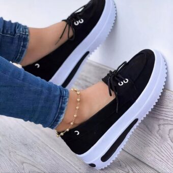 Photo of a pair of black platform loafers worn by a woman in jeans, on a parquet floor and white wall