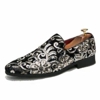 On a white background, a profile moccasin in black velvet with floral embroidery in silver thread and sequins. The sole is black and there's a wooden shoe tree inside, with a gilded metal shank at the heel.