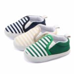 On a white background, 3 black, beige and green striped baby moccasins with white sole and elasticated sides