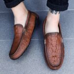 Photo of a pair of brown moccasins worn by a woman with black pants on a gray floor