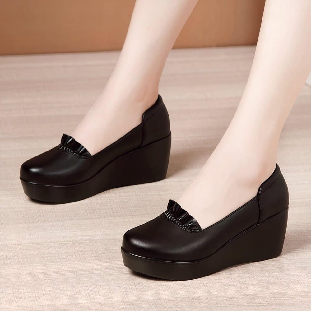 Photo of a pair of black wedge loafers worn by a woman on a parquet floor with a brown wall in the background